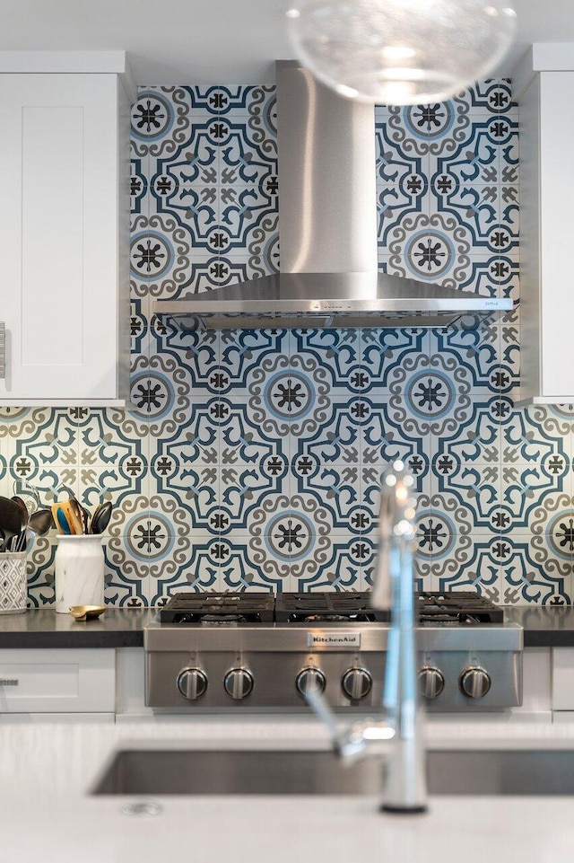 details featuring white cabinets, decorative backsplash, stainless steel gas stovetop, and wall chimney exhaust hood