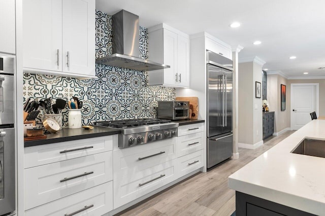 kitchen with white cabinetry, wall chimney exhaust hood, light hardwood / wood-style floors, crown molding, and appliances with stainless steel finishes