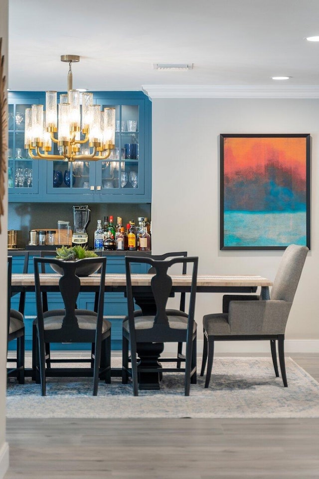 bar featuring ornamental molding, pendant lighting, blue cabinetry, and an inviting chandelier