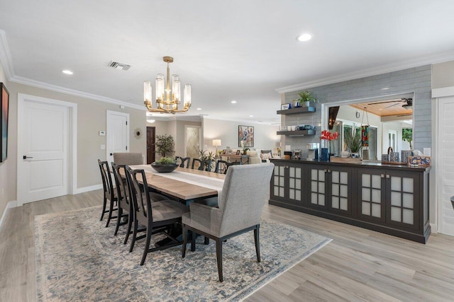 dining room with ceiling fan with notable chandelier, light wood-type flooring, and crown molding