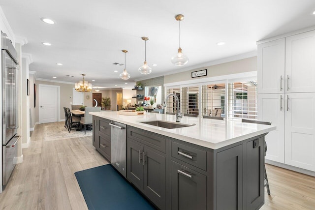 kitchen with white cabinets, a kitchen island with sink, crown molding, pendant lighting, and sink