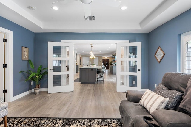 living room featuring sink, french doors, ceiling fan, light hardwood / wood-style floors, and a tray ceiling