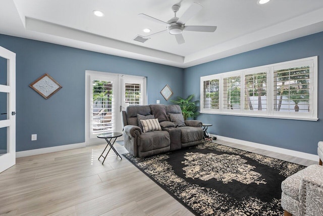 living room featuring ceiling fan, light hardwood / wood-style flooring, french doors, and a raised ceiling