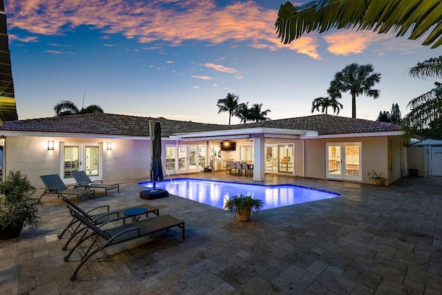 pool at dusk featuring french doors and a patio area