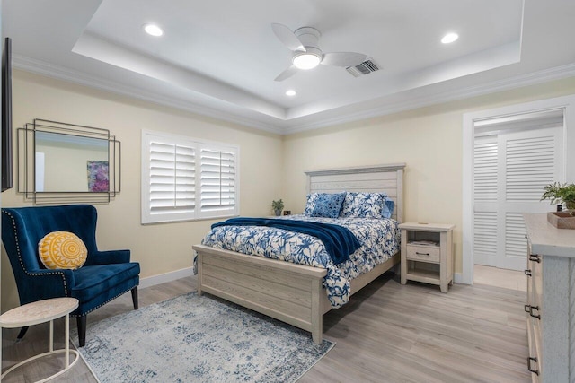 bedroom with ceiling fan, light hardwood / wood-style floors, crown molding, and a tray ceiling