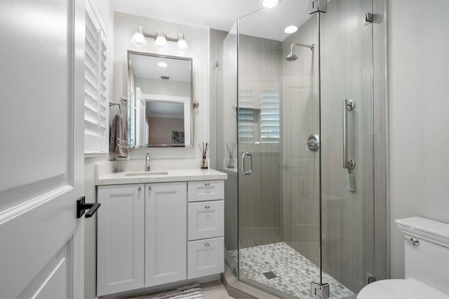 bathroom featuring toilet, a shower with shower door, and vanity