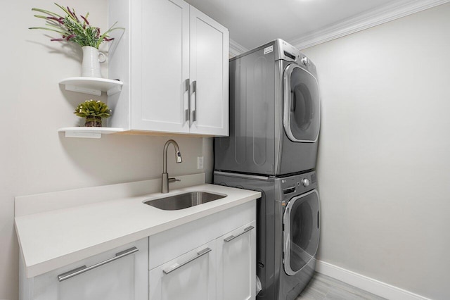 clothes washing area with sink, stacked washer and dryer, crown molding, and cabinets