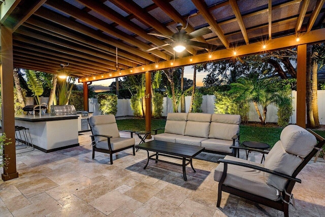 patio terrace at dusk featuring ceiling fan, exterior bar, and outdoor lounge area