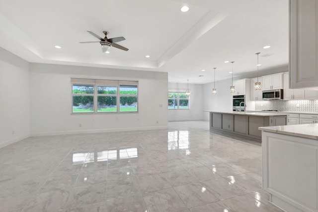 unfurnished living room with a raised ceiling, ceiling fan, and sink