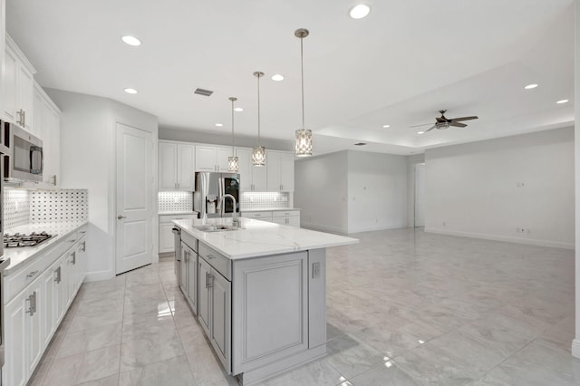 kitchen with decorative backsplash, a kitchen island with sink, sink, pendant lighting, and white cabinets