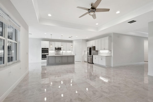 kitchen featuring a tray ceiling, white cabinetry, a center island with sink, and stainless steel appliances