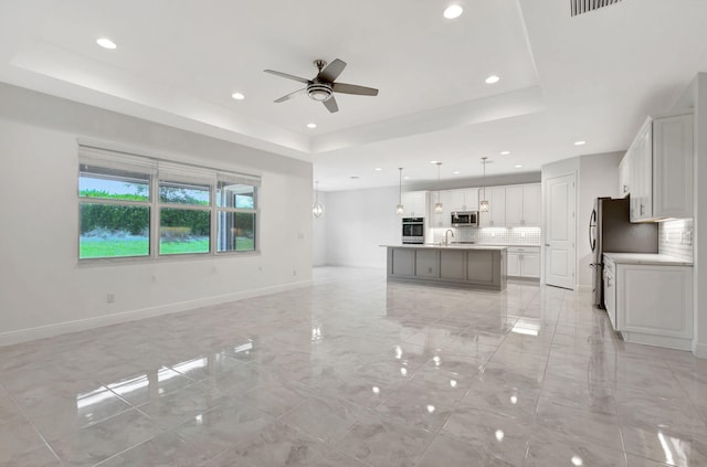 kitchen with backsplash, stainless steel appliances, a raised ceiling, hanging light fixtures, and an island with sink