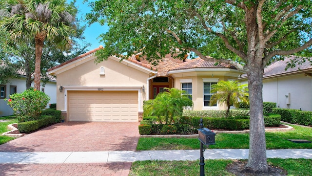 mediterranean / spanish-style house with decorative driveway, a tiled roof, an attached garage, and stucco siding