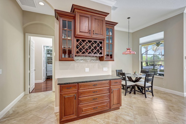 kitchen with light tile patterned floors, dark stone counters, hanging light fixtures, and crown molding