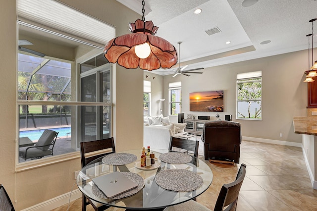 tiled dining space featuring a raised ceiling, ceiling fan, plenty of natural light, and ornamental molding