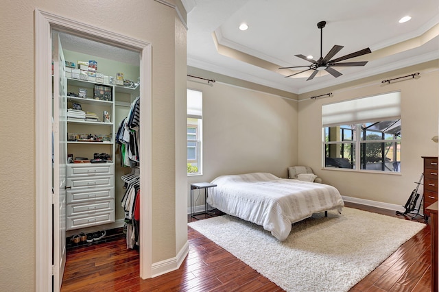 bedroom featuring ceiling fan, dark wood-type flooring, a tray ceiling, a closet, and ornamental molding