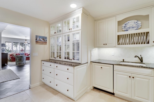 kitchen with backsplash, dark stone counters, sink, white cabinets, and light parquet flooring