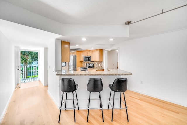 kitchen with stainless steel appliances, tasteful backsplash, light hardwood / wood-style flooring, kitchen peninsula, and a kitchen bar