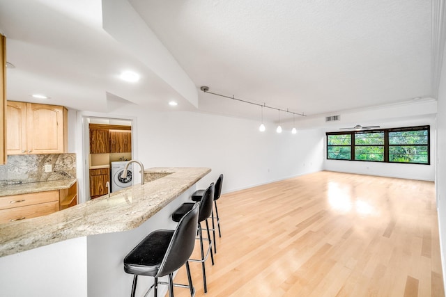 kitchen featuring tasteful backsplash, washer / clothes dryer, track lighting, a breakfast bar area, and light brown cabinetry