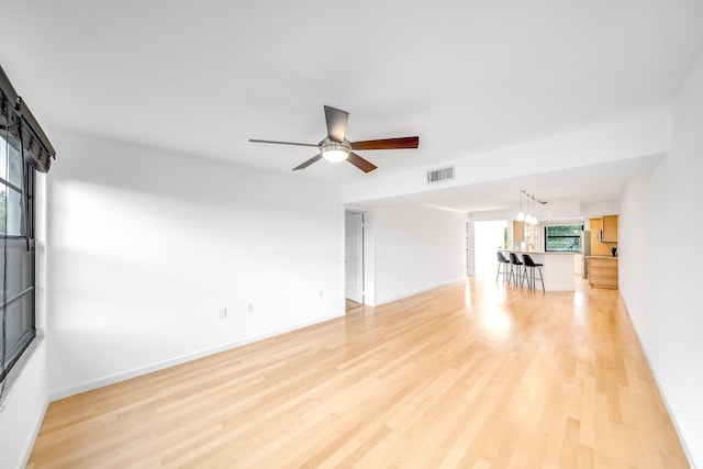 empty room with ceiling fan with notable chandelier and light wood-type flooring