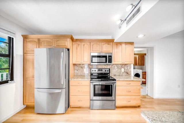 kitchen with light brown cabinets, light stone counters, washer / dryer, appliances with stainless steel finishes, and light wood-type flooring