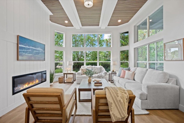 living room with beam ceiling, wood ceiling, a high ceiling, and light hardwood / wood-style flooring