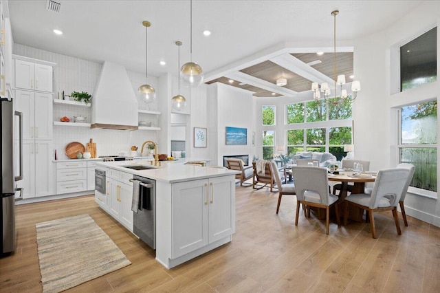 kitchen featuring pendant lighting, a kitchen island with sink, white cabinets, custom range hood, and appliances with stainless steel finishes