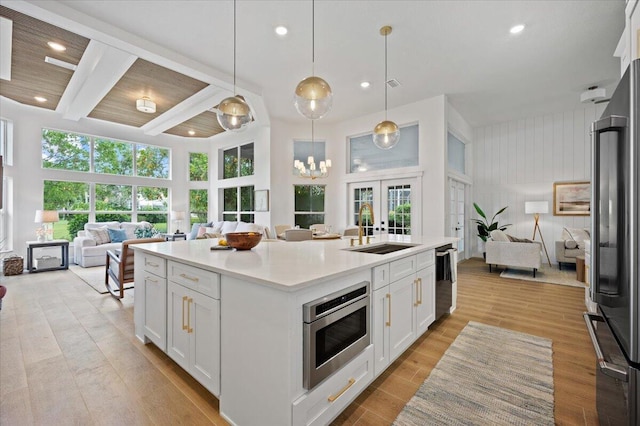 kitchen with white cabinetry, sink, beamed ceiling, decorative light fixtures, and a kitchen island with sink