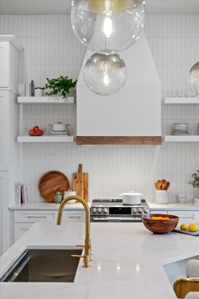 kitchen with white cabinetry, light stone countertops, sink, decorative backsplash, and stainless steel stove