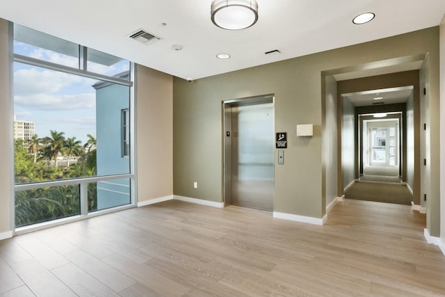 unfurnished room with light wood-type flooring, elevator, floor to ceiling windows, and a healthy amount of sunlight