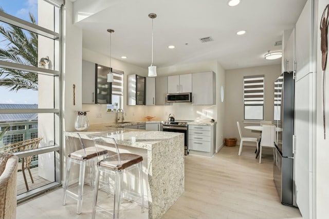 kitchen with light stone countertops, hanging light fixtures, kitchen peninsula, gray cabinets, and appliances with stainless steel finishes