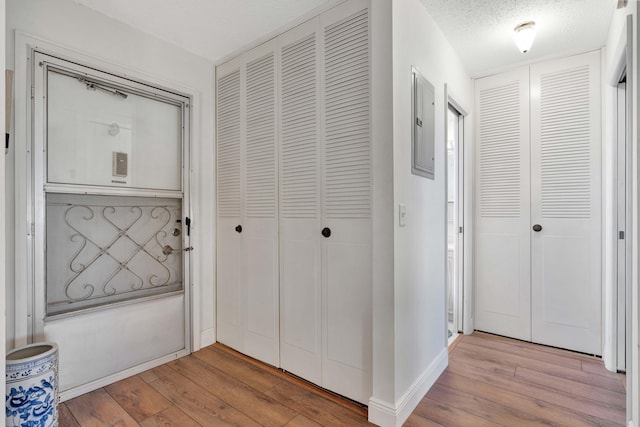 hall with a textured ceiling, electric panel, and light hardwood / wood-style flooring