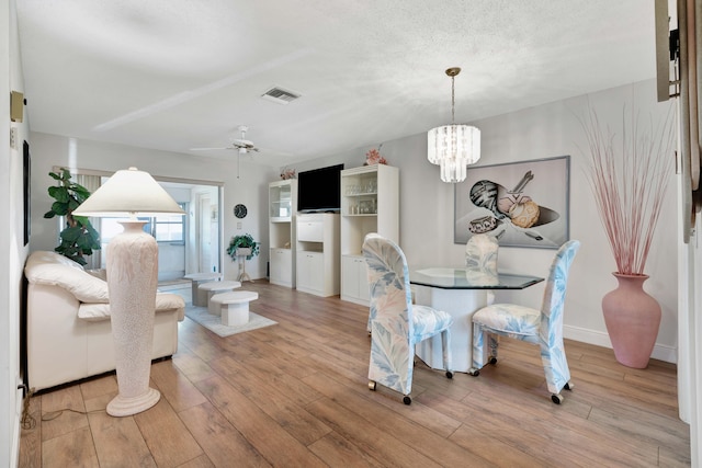 dining area with a textured ceiling, ceiling fan with notable chandelier, and light hardwood / wood-style flooring