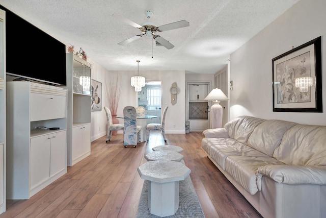 living room featuring light hardwood / wood-style flooring, ceiling fan with notable chandelier, and a textured ceiling