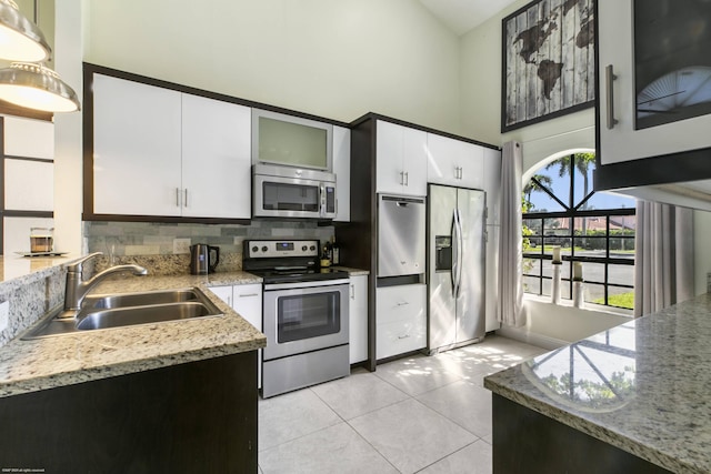 kitchen with sink, white cabinetry, a towering ceiling, stainless steel appliances, and light stone countertops