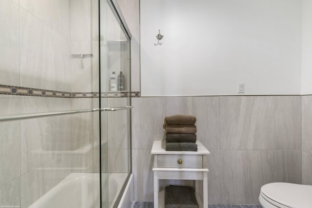 bathroom with toilet, shower / bath combination with glass door, and tile walls