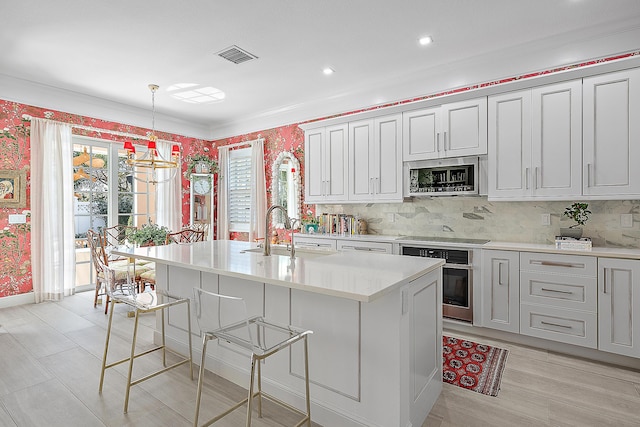 kitchen with pendant lighting, a breakfast bar, a kitchen island with sink, sink, and appliances with stainless steel finishes