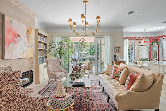 living room with french doors, an inviting chandelier, crown molding, wood walls, and a textured ceiling