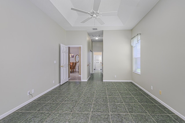 empty room featuring dark tile patterned floors, a raised ceiling, and ceiling fan