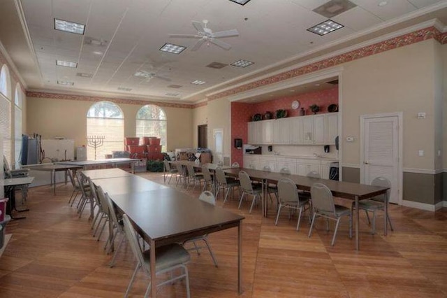 dining room featuring crown molding, light hardwood / wood-style flooring, ceiling fan, and a towering ceiling