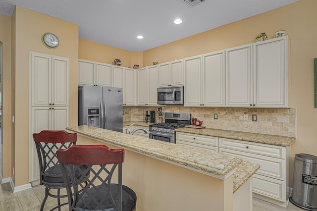 kitchen featuring tasteful backsplash, appliances with stainless steel finishes, a kitchen bar, and light stone countertops