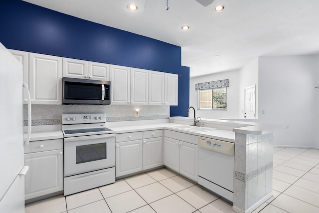 kitchen featuring a peninsula, white appliances, a sink, and white cabinets