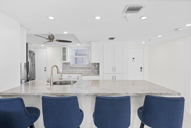 kitchen with stainless steel fridge, light stone counters, ceiling fan, sink, and white cabinetry