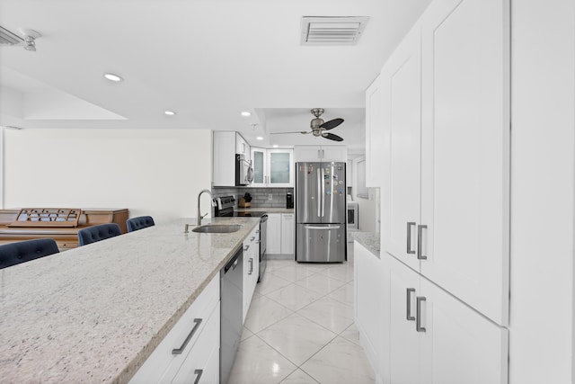 kitchen featuring ceiling fan, decorative backsplash, light stone countertops, appliances with stainless steel finishes, and white cabinetry