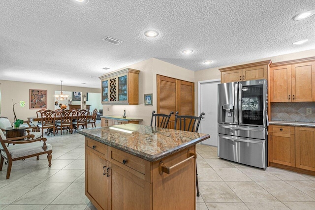 kitchen featuring a center island, stainless steel refrigerator with ice dispenser, a notable chandelier, pendant lighting, and dark stone counters