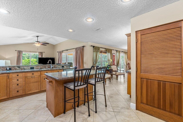 kitchen featuring a breakfast bar area, ceiling fan, light tile patterned flooring, and vaulted ceiling