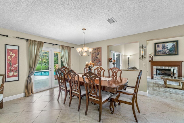 tiled dining space featuring a textured ceiling, a notable chandelier, a fireplace, and french doors