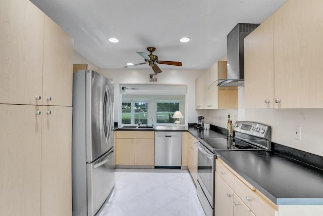 kitchen with dark countertops, stainless steel appliances, wall chimney range hood, light brown cabinets, and a sink