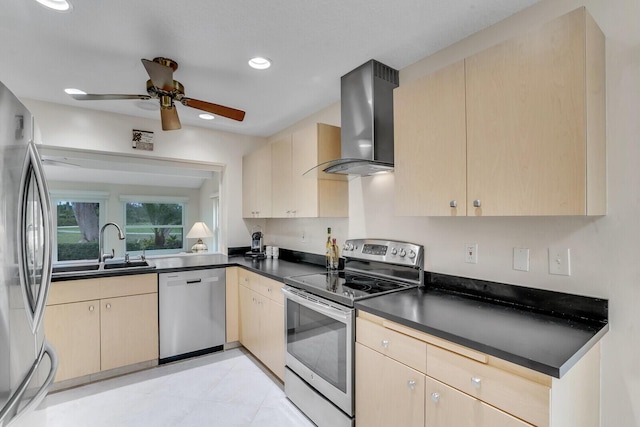 kitchen with light brown cabinets, stainless steel appliances, a sink, wall chimney exhaust hood, and dark countertops