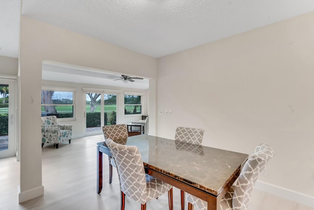 dining space featuring a ceiling fan, light wood-type flooring, a textured ceiling, and baseboards